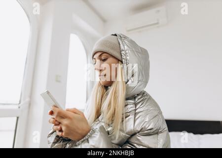 Frau trägt Winterjacke mit Handy zu Hause Stockfoto