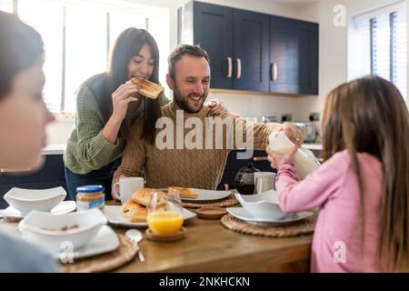 Glücklicher Mann und glückliche Frau frühstücken mit Kindern in der Küche Stockfoto