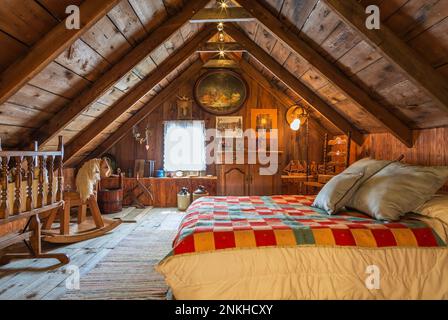 Queen-Size-Bett mit bunten gesteppten Wolldecken und antiker Holzschränke, Kinderbett, Schaukelpferd und Stuhl im Sommer Hauptschlafzimmer im alten Haus aus den 1840 Jahren. Stockfoto