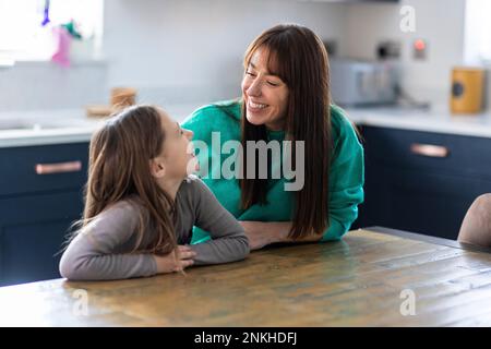 Lächelnde Mutter und Tochter, die an einem Tisch in der Küche sitzen Stockfoto