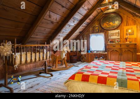 Queen-Size-Bett mit bunten gesteppten Wolldecken und antiker Holzschränke, Kinderbett und schaukelndem Pferd im Sommer Hauptschlafzimmer im alten 1840-Jahre-Haus. Stockfoto