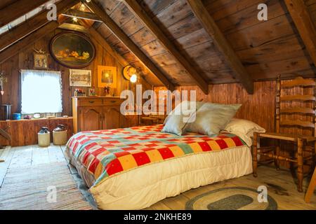 Queen-Size-Bett mit bunter gesteppter Wolldecke und antiker Holzschränke, Stühle im Sommer Hauptschlafzimmer auf der oberen Etage im alten 1840-Haus. Stockfoto