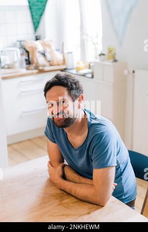 Lächelnder reifer Mann, der zu Hause am Esstisch sitzt Stockfoto