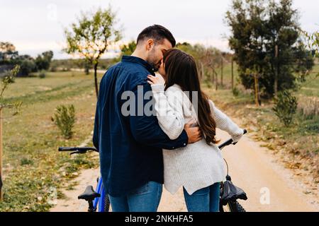 Romantisches Paar mit Fahrrädern, die sich auf einer unbefestigten Straße küssen Stockfoto