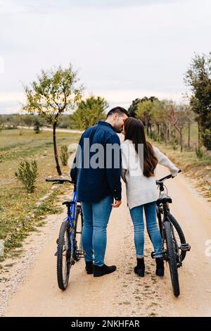 Ein junges Paar mit Fahrrädern, das sich auf einer unbefestigten Straße küsst Stockfoto