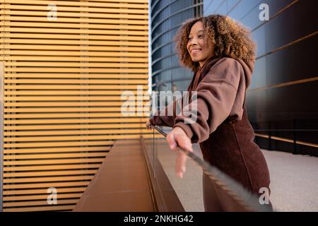 Junge Frau, die sich an ein Glasgeländer lehnt Stockfoto