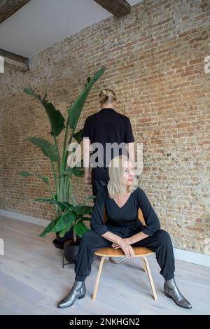 Eine Frau, die auf einem Stuhl sitzt, von einem Mann gegenüber der Ziegelwand Stockfoto