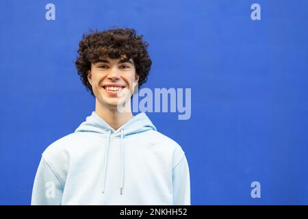 Lächelnder junger Mann, der vor der blauen Wand steht Stockfoto