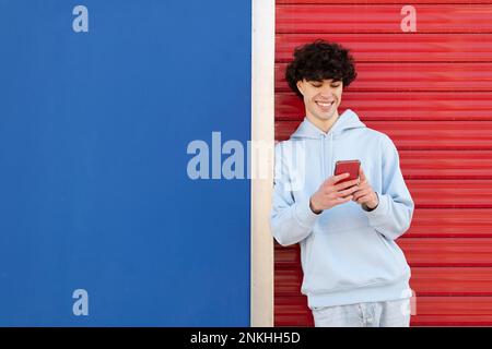 Glücklicher Mann mit Smartphone, der vor einer zweifarbigen Wand steht Stockfoto