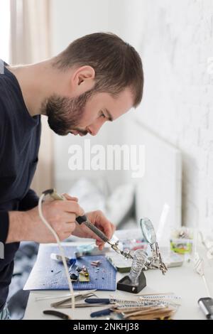 Techniker, der Geräte mit Lötkolben in der Werkstatt repariert Stockfoto