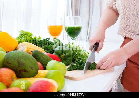 Hände mit einem Messer schneiden Gemüse über Holz Schnitzbrett auf dem Tisch auf weißem Vorhang Hintergrund Stockfoto