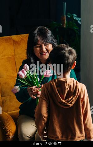 Glückliche Großmutter, die Enkelsohn zu Hause Tulpenblüten schenkt Stockfoto