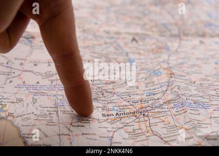 Nahaufnahme eines Fingers, der auf einer detaillierten, farbenfrohen Karte mit selektivem Fokus, geringer Schärfentiefe und Unschärfe im Hintergrund nach San Antonio, Texas zeigt Stockfoto