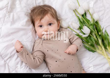 Niedliches Baby mit weißen Tulpen auf der Decke, Banner, Platz für Text. Hochwertiges Foto Stockfoto