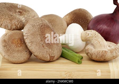 Shiitake-Pilze und verschiedene Zwiebelsorten auf einem Holzschneidbrett auf weißem Hintergrund. Rezepte und Heilkräuter Stockfoto