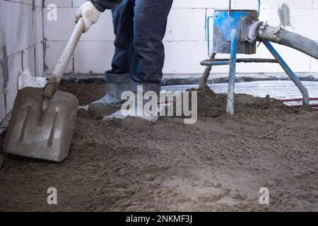 Halbtrockene Bodenbohle – ein Arbeiter schaufelt eine Baumischung durch eine spezielle Hülse zum Zementieren und Nivellieren von Fußbodenheizungsrohren. Stockfoto