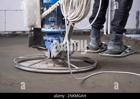 Rampfen und Schleifen von halbtrockenem Boden, der von einer Maschine mit rotierender Scheibe zum Nivellieren bearbeitet wird. Bau eines Betonfußbodens im Haus, ein Meister Stockfoto