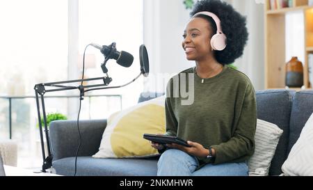 Coole Afro-Journalistin, die ein digitales Tablet verwendet, in das Mikrofon spricht und Podcasts oder Nachrichten überträgt, während sie Kopfhörer trägt. Aufgeregt, jung Stockfoto