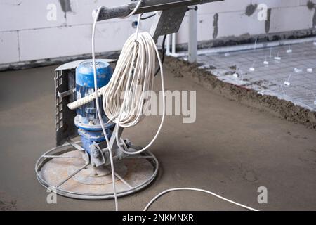 Rampfen und Schleifen von halbtrockenem Boden, der von einer Maschine mit rotierender Scheibe zum Nivellieren bearbeitet wird. Bau eines Betonfußbodens im Haus, ein Meister Stockfoto