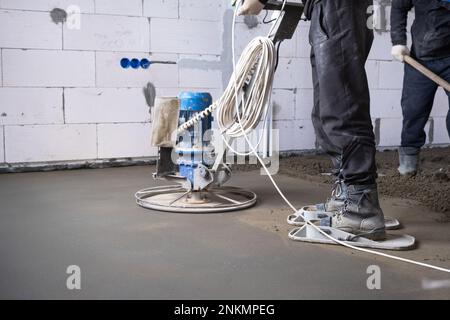 Rampfen und Schleifen von halbtrockenem Boden, der von einer Maschine mit rotierender Scheibe zum Nivellieren bearbeitet wird. Bau eines Betonfußbodens im Haus, ein Meister Stockfoto