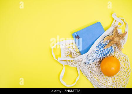 Notizbuch mit Seesternen und Orange mit Tasche mit Schnur auf gelbem Hintergrund. Konzept von Urlaub, Reisen, Sommer in heißen Ländern. Speicherplatz kopieren Stockfoto