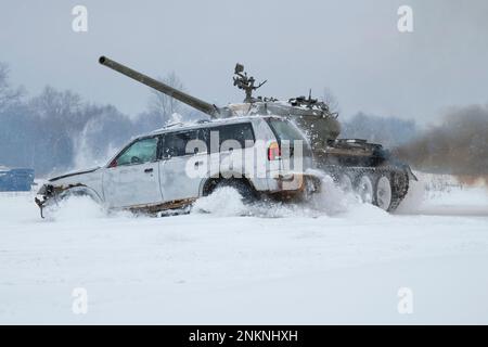 KRASNOYE SELO, RUSSLAND - 19. FEBRUAR 2023: Ein sowjetischer Panzer T-54 rammt einen alten Pkw an einem verschneiten Februar-Tag. Panzershow in der Militärgeschichte p Stockfoto