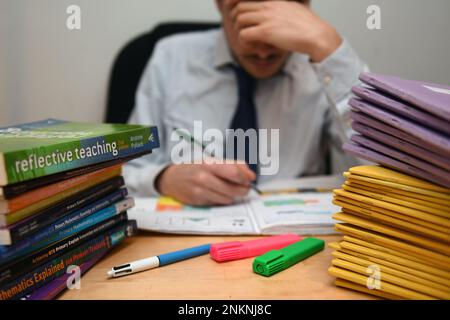 Ein Dateifoto vom 05. Dezember 03/17, auf dem ein Grundschullehrer neben einem Haufen von Klassenbüchern gestresst wirkte, als die Beschäftigten des öffentlichen Sektors nach Millionen unbezahlter Überstunden im letzten Jahr „ausgebrannt“ wurden und ihren Arbeitsplatz kündigten, laut einem Bericht. Stockfoto