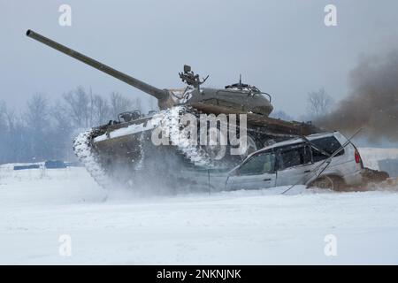 KRASNOYE SELO, RUSSLAND - 19. FEBRUAR 2023: Ein sowjetischer Panzer T-54 zerquetscht einen alten Pkw auf einem verschneiten Feld. Panzershow im historischen Militärpark Stockfoto