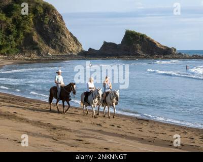 Drei Personen auf dem Pferderücken genießen eine Fahrt am Strand von Samara Costa Rica Stockfoto