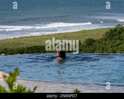 Eine Frau schwimmt in einem Infinity-Pool mit Blick auf das Meer in Nosara Costa Rica Stockfoto