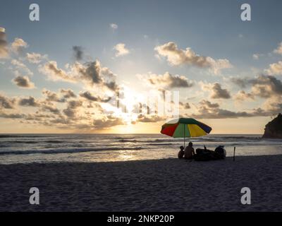 Eine Familie genießt die letzte Sonne im Schatten eines bunten Sonnenschirms an einem Strand nahe Nosara in Costa Rica Stockfoto