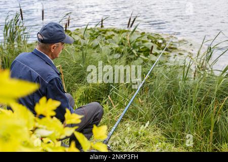 Fischer lehnen sich mit einer Angelrute am Ufer des Sees zurück und fangen Fische. Stockfoto