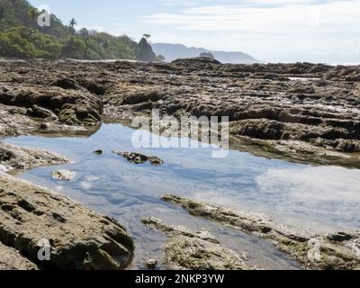 Felsen und Felsenpools voller Wasser am Strand in Playa Hermosa in Costa Rica Stockfoto