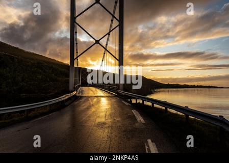 Brücke über den Fluss im Norden Norwegens im wunderschönen Sonnenuntergang oder Sonnenaufgang im Hintergrund Stockfoto