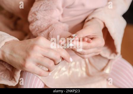 Eine Frau schneidet ihrer kleinen Tochter zu Hause die Nägel durch Stockfoto