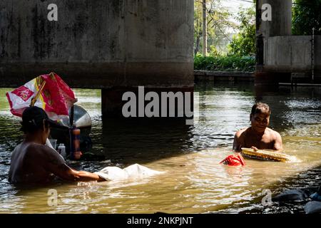 Lad Krabang, Thailand, 24/02/2023, Eine Familie waten durch den Kanal, während sie nach Münzen und Krabben Beanath eine Unterführung. Das tägliche Leben rund um Lad Krabang, ein Wohnviertel in der Nähe des internationalen Flughafens Suvarnabhumi, in East Bangkok, Thailand, am 24. Februar 2022. Stockfoto