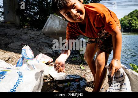 Lad Krabang, Thailand, 24/02/2023, Ein Junge zeigt eine winzige Krabbe, die er im Kanal gefunden hat. Das tägliche Leben rund um Lad Krabang, ein Wohnviertel in der Nähe des internationalen Flughafens Suvarnabhumi, in East Bangkok, Thailand, am 24. Februar 2022. Stockfoto