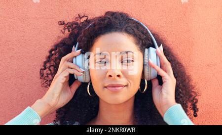 Musik, Kopfhörer und Gesicht einer glücklichen schwarzen Frau, die vor einem Hintergrund Radio, Lieder und Geräusche hört. Afrikanischer weiblicher Kopf in Funktechnik Stockfoto