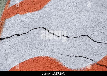 Zwei große, gewundene, absteigende Risse auf einer alten, farbigen Putzwand. Speicherplatz kopieren. Selektiver Fokus. Stockfoto