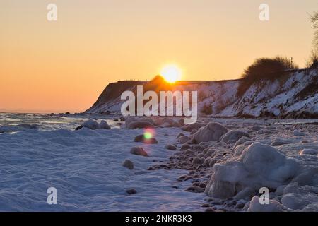 Sonnenuntergang an einem verschneiten Strand hinter einem Hügel, der Himmel scheint in goldenen und pfirsichfarbenen Orange Farben. Stockfoto