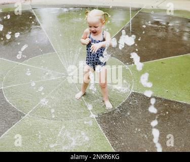 Ein junges Mädchen, das im Wasserbrunnen im Park spielt Stockfoto