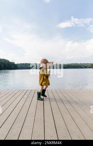 Ein junges Mädchen mit gummistiefeln und Hut auf der Terrasse neben dem See Stockfoto