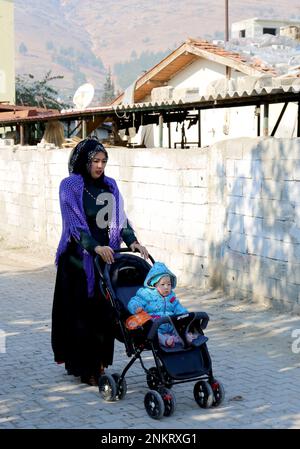 OVAKENT, HATAY, TÜRKEI-DEZEMBER 10: Unidentifizierte usbekische Frau mit Sohn auf Stroller, der die Straße entlang läuft. Dezember 10,2016 in Ovakent, Hatay, Türkei Stockfoto