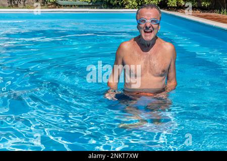 Ein weißer Mann mittleren Alters mit Schwimmbrille schreit fröhlich in einem Swimmingpool Stockfoto