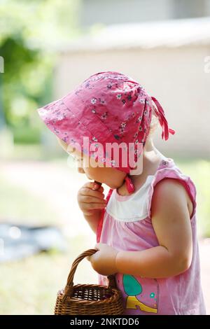 Gesunder Lebensstil, kleines Mädchen im Garten mit einem Korb frischer Kirschen schmeckt nach roten Beeren. Mahlzeiten für Kinder mit frischen Beeren aus dem g Stockfoto