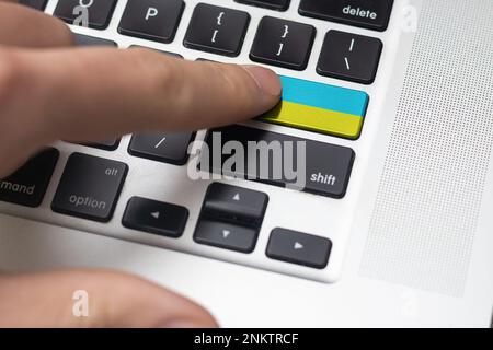 Durch Drücken der Eingabetaste mit ukrainischer Flagge wird ein Cyberangriff auf die Ukraine dargestellt, eine Metapher des Erlernens ukrainischer Sprache, schwarze Tastatur, Nahaufnahme, Vorderseite Stockfoto