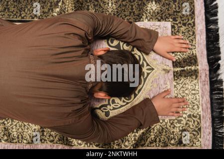 Draufsicht eines muslimischen Jungen, der zu Hause auf dem Teppich betet, Bild der Börse Stockfoto