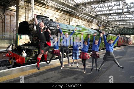 Piper Kevin MacDonald von den Red Hot Chilli Pipers mit Schulkindern von der Royal Scottish Country Dance Society, während einer Veranstaltung am Bahnhof Edinburgh Waverley anlässlich des Tages, als die weltberühmte Lokomotive Flying Scotsman am 24 1923. Februar in Betrieb ging. Foto: Freitag, 24. Februar 2023. Stockfoto