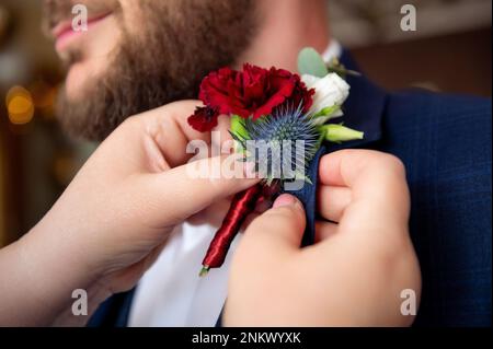 Blumen, Blumensträuße, Blumensträuße, rote Blüten in Blüten und marineblauer Jacke, mom, die das Blütenstumpf ihres Sohnes steckt Stockfoto
