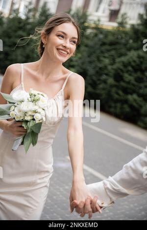 Bräutigam hält Hand der glücklichen Braut in weißem Kleid mit Hochzeitsstrauß, Stockbild Stockfoto